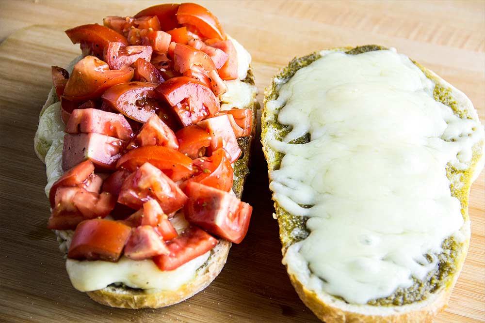 Adding Tomato Pieces to Melted Cheese on Italian Bread