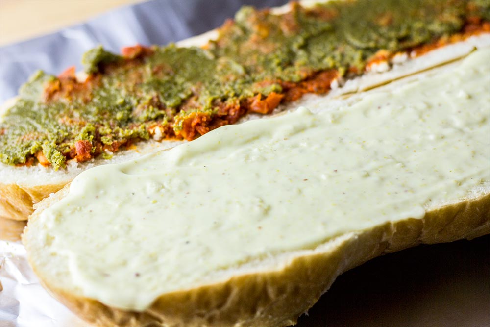 Applying Sun Dried Tomato Spread, Basil Pesto & Mayonnaise to French Bread